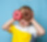 Little happy cute boy is eating donut on blue background wall. child is having fun with do