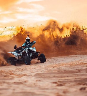 Person driving ATV through desert sand dune at sunset