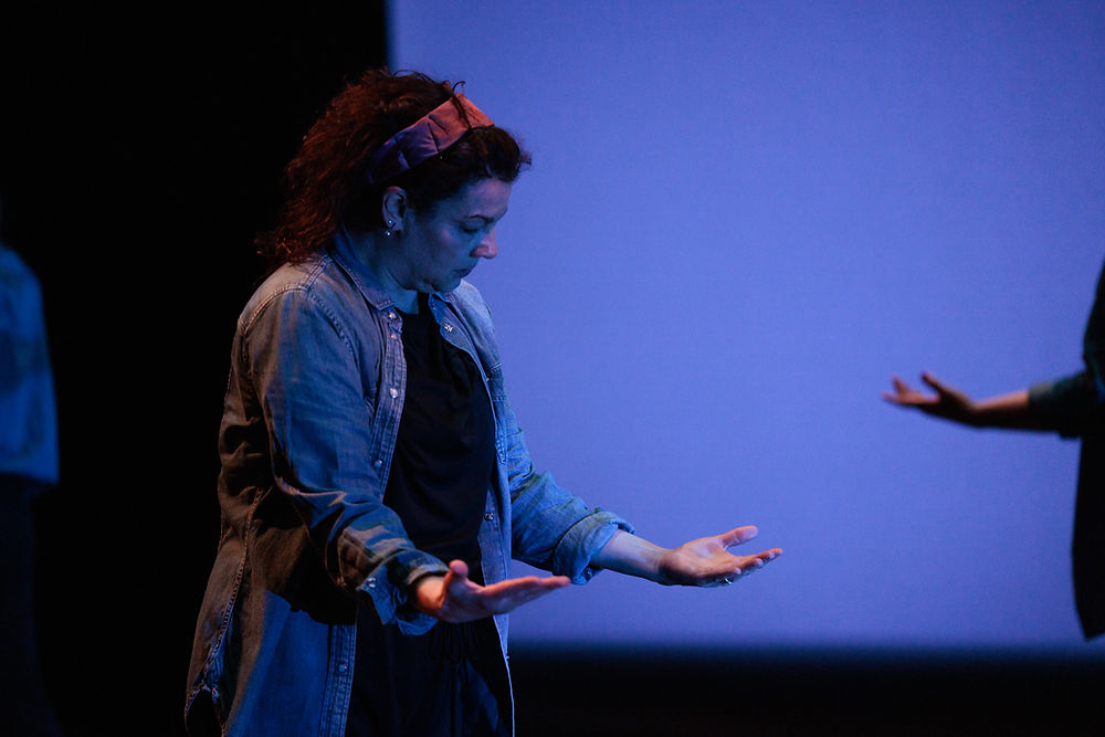 Dancer in denim button down top and red headband, staring down at outstretched hands.
