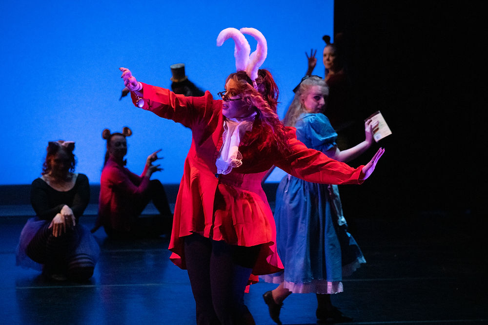 Dancer in red coat with white bunny ears, a scene from an Alice In Wonderland inspired dance