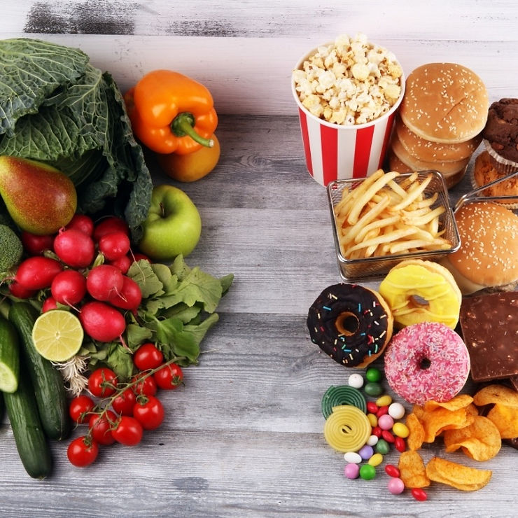Healthy food swaps at work — fresh vegetables and fruit on one side versus fast food, chips, and sweets on the other, highlighting better workplace nutrition choices.