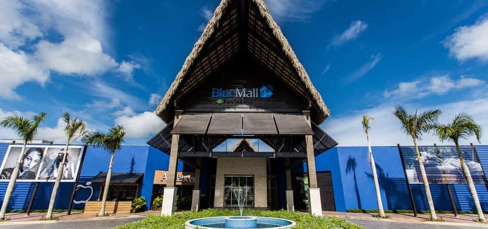 iew of BlueMall Puntacana's exterior at sunset, with bright lights and visitors heading into the shopping center for a unique retail experience in the Dominican Republic.