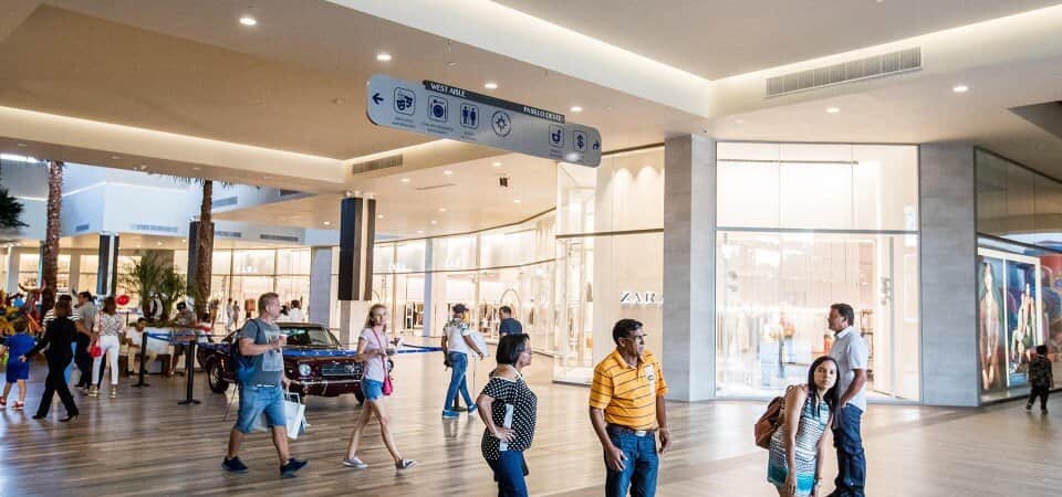 Wide-angle view of the BlueMall Puntacana entrance, with shoppers walking under the sun and a variety of high-end shops and restaurants in sight