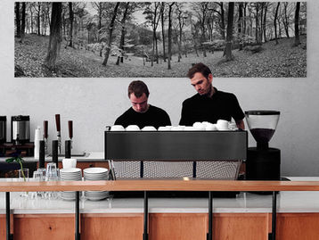 barista an theke mit schwarz weißem Panoramafoto von Buchenwald im Hintergrund