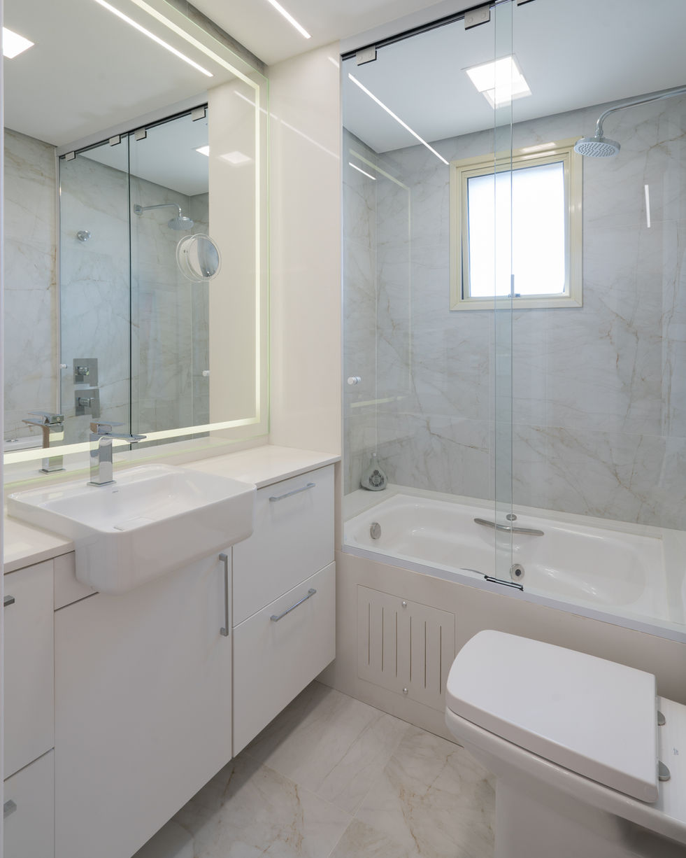 Banheiro com estética de spa, apresentando paredes e piso em revestimento marmorizado claro. Em destaque, uma banheira de hidromassagem moderna e uma bancada com espelho iluminado por LED frontal, criando um ambiente clean, sofisticado e bem iluminado.