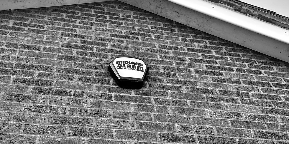 a black and white image of a midland alarm east, wireless bell box installed on the outside apex of a brick built home in Northamptonshire