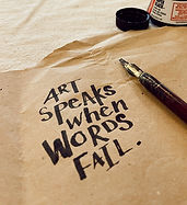 Photo of a dip pen lying on top of brown paper. Nest to the pen is the handwritten quote saying "Art speaks when words fail."