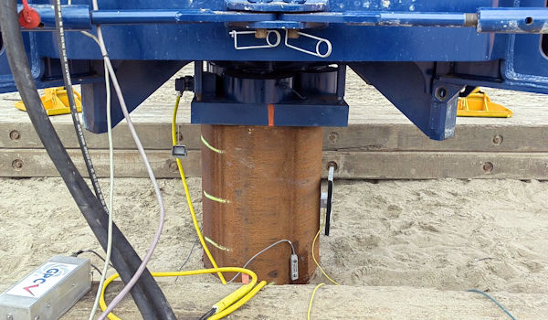 A vibrating hammer drives a tube pile into the ground, which is monitored by the GPC PDA system.