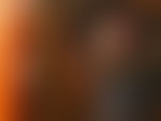 A decaying zombie woman in a torn dress leans against a wooden-paneled wall, clawing at a cracked family portrait. Warm orange light bleeds in from the side, contrasting with the dark, eerie tones of her bloodied skin and matted hair. A smaller faded photo hangs nearby, heightening the sense of loss and dread.
