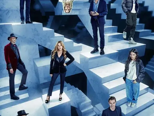 Promotional image for Now You See Me: Now You Don’t (2025), showing the ensemble cast standing on an M.C. Escher–style staircase maze of blue marble blocks, with one character hanging upside down. The visual illusion theme highlights the film’s focus on magic, deception, and perspective.