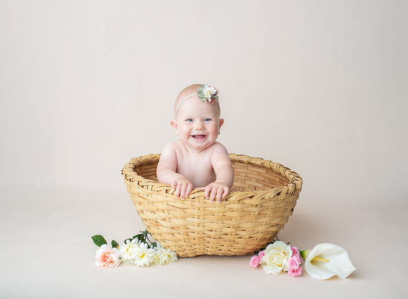 little baby sitting in a large round basket with a big smile and flowers