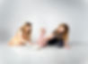 Little girl's first birthday cake smash. Her two eight-year old sisters are helping her eat the cake while they sit on a reflective white backdrop for their photogrpaher mom.