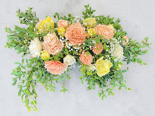 Peach and yellow wood flower arrangement with greenery on a concrete surface.