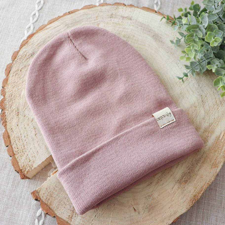 Blush knit toque with Onyx & Ivy logo tag, styled on wood round with greenery.