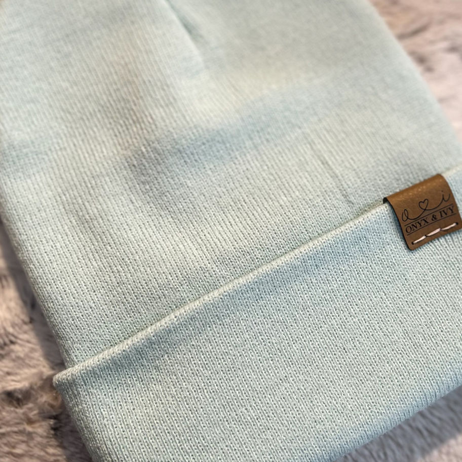 Sky coloured knit toque with Onyx & Ivy logo tag, folded and displayed on a soft textured background.