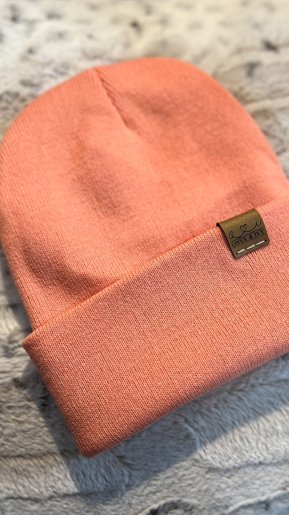 Coral knit toque with Onyx & Ivy logo tag, folded and displayed on a soft textured background.