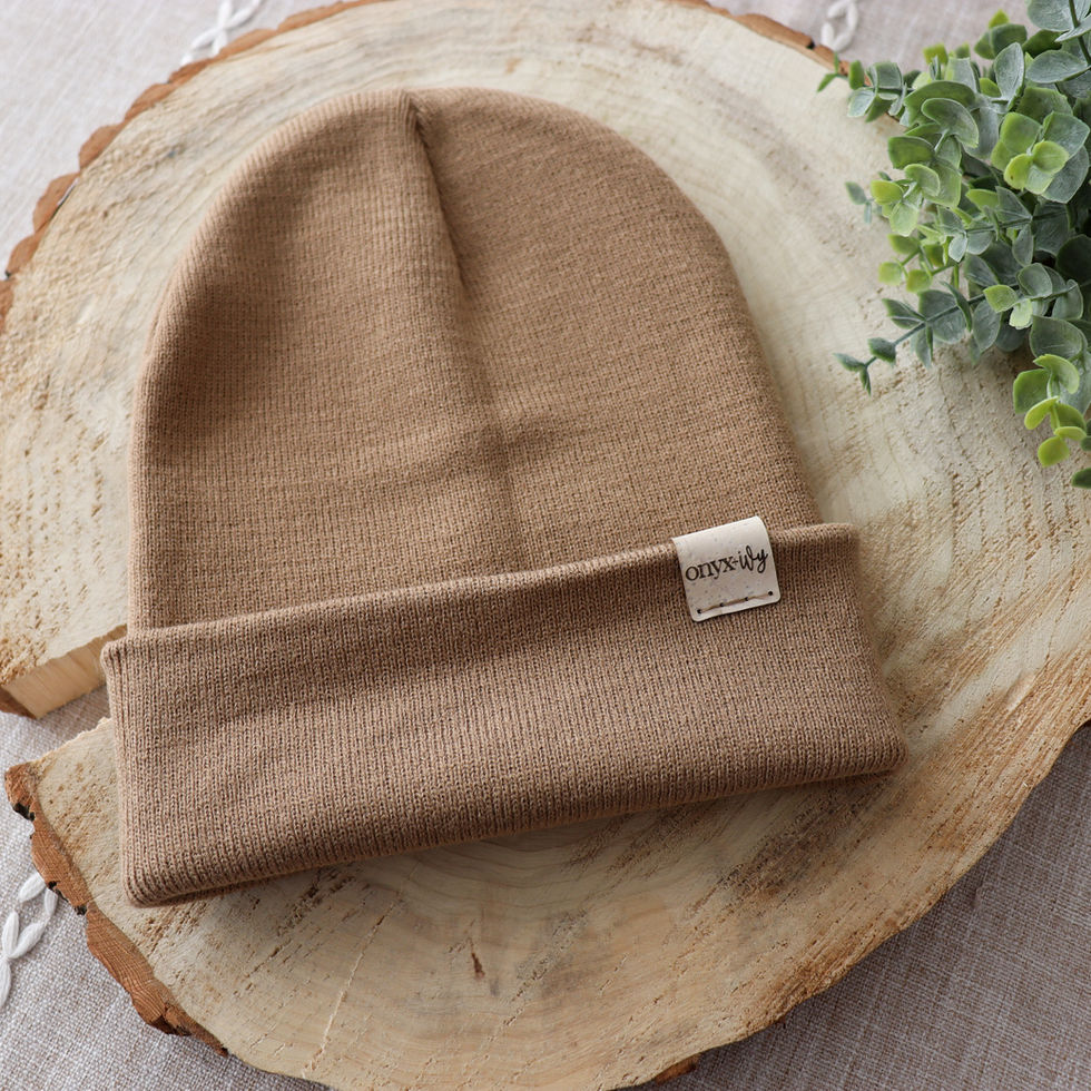 Camel knit toque with Onyx & Ivy logo tag, styled on wood round with greenery.