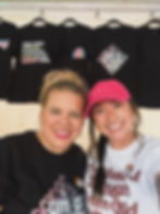 Two smiling women from Onyx & Ivy wearing activist apparel at a market booth. One wears a black shirt with rainbow earrings,