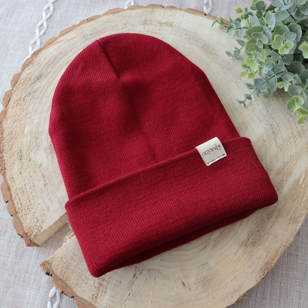 Dark red knit toque with Onyx & Ivy logo tag, styled on wood round with greenery.