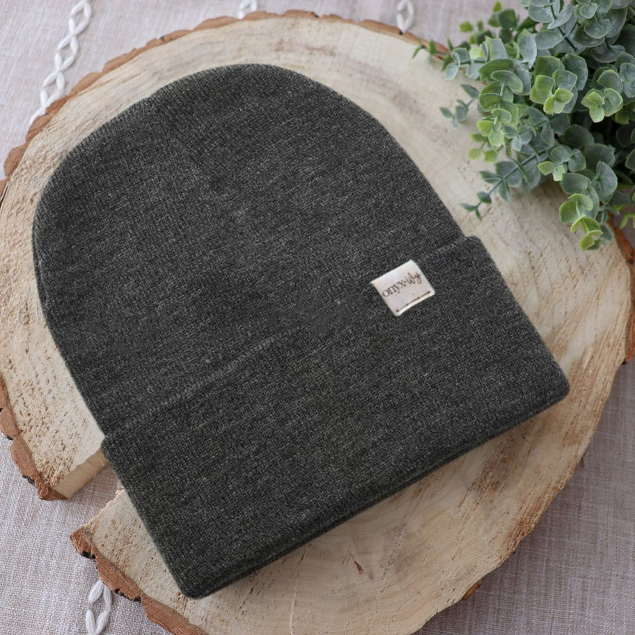 Charchoal knit toque with Onyx & Ivy logo tag, styled on wood round with greenery.
