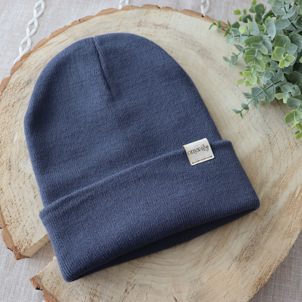 Denim knit toque with Onyx & Ivy logo tag, styled on wood round with greenery.