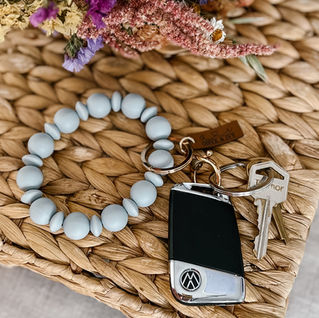 Blue beaded wristlet keychain with keys and fob on woven mat with dried florals.