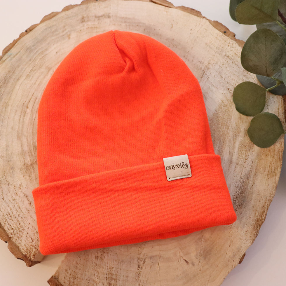 Neon orange knit toque with Onyx & Ivy logo tag, styled on wood round with greenery.