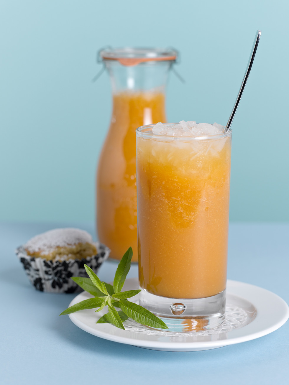 Fruchtsaft im Glas mit Eis und Muffin im Hintergrund