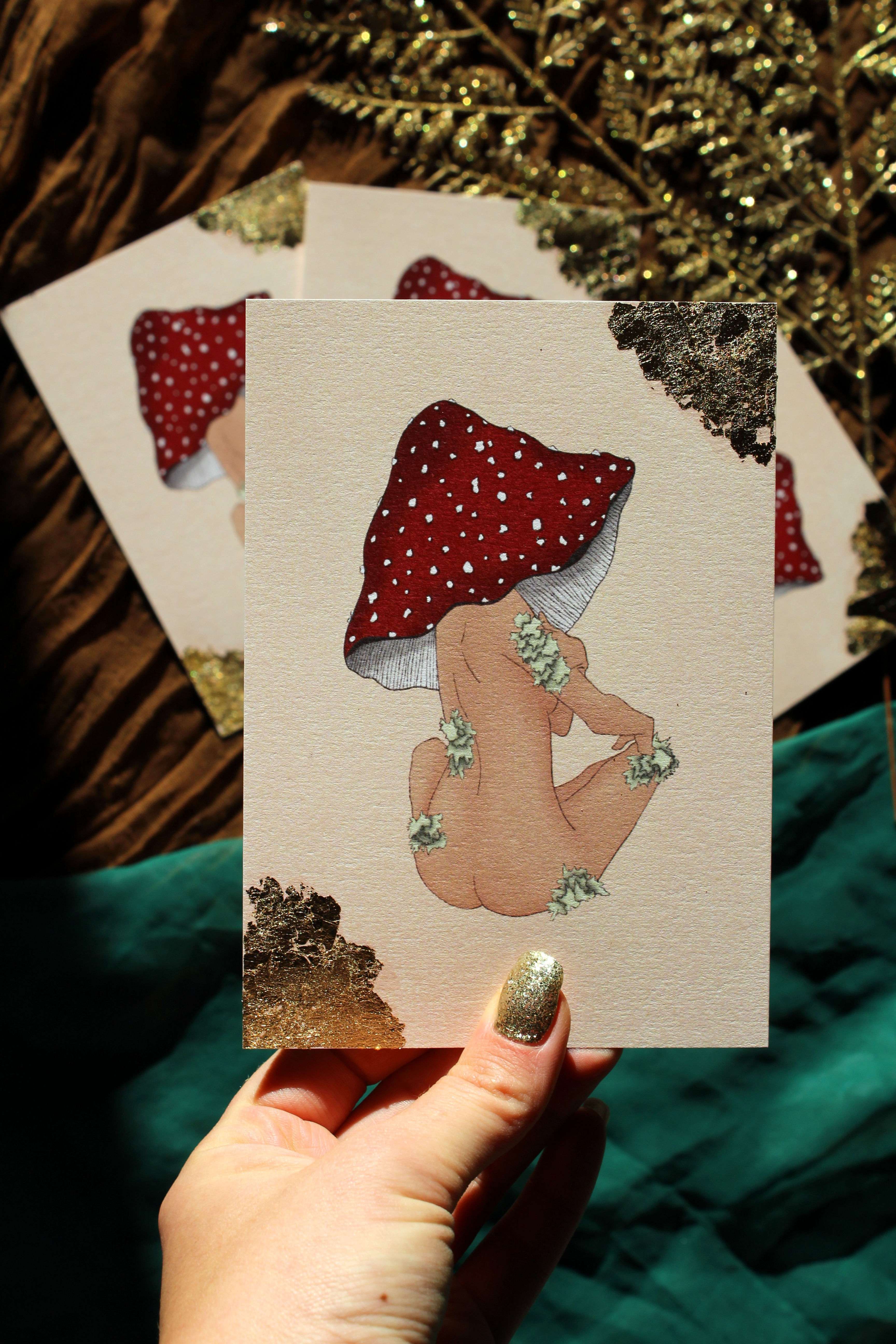 Carte illustrée “Femme Champignon” posée sur une surface avec éléments naturels, lumière dorée