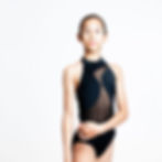 Dancer in black halter leotard featuring curved sheer front panel, looking upward against white background.
