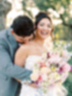 A bride laughs at the camera while her groom smiles and kisses her on her shoulder at their colorful