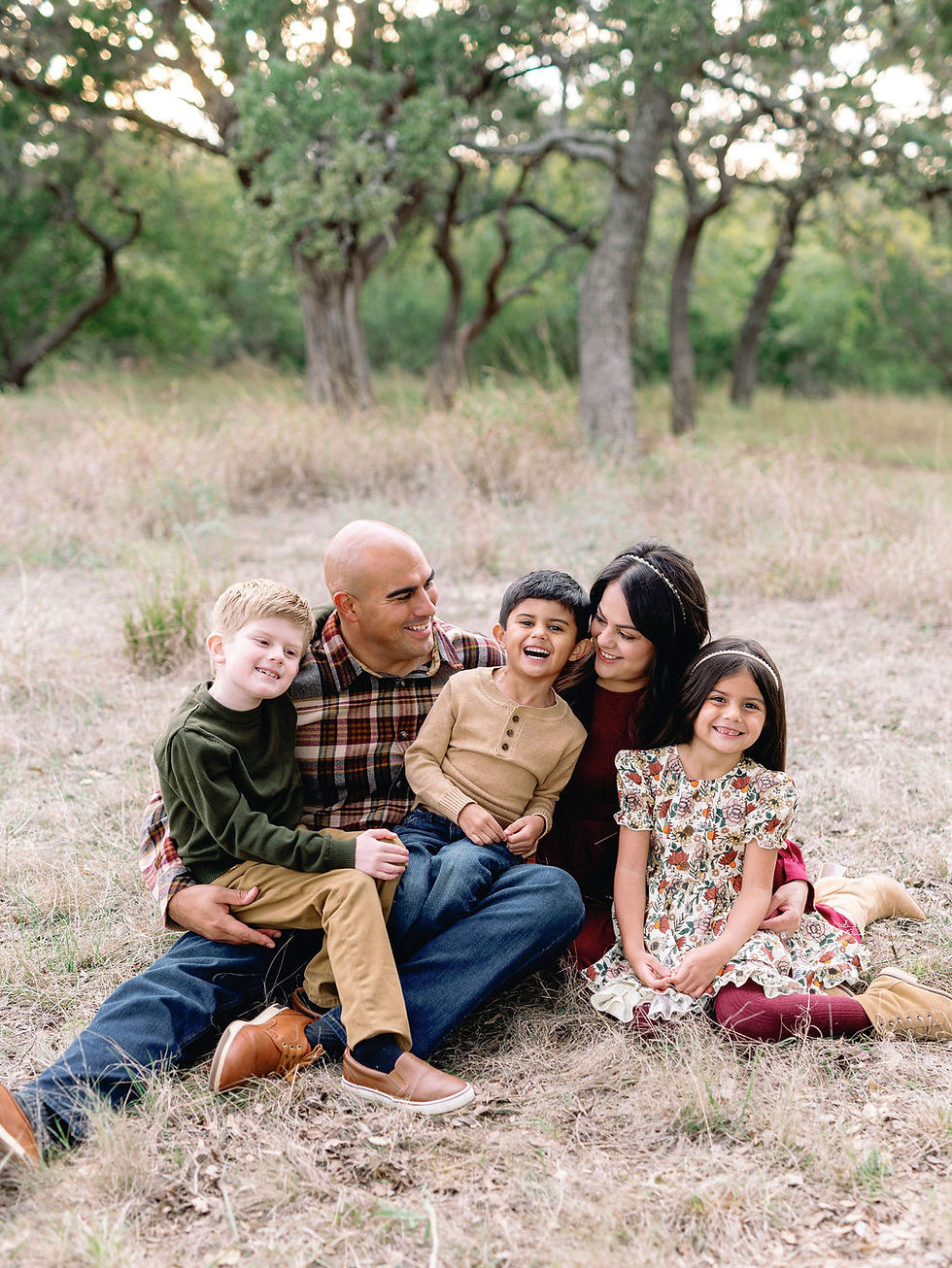 Family of five sitting together in a grassy field during a fall photo session near New Braunfels, TX
