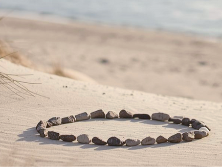 Circle of stones on sandy beach, surrounded by grasses, with a calm sea in the background. Serene and peaceful atmosphere. Represents how plan is start to work.
