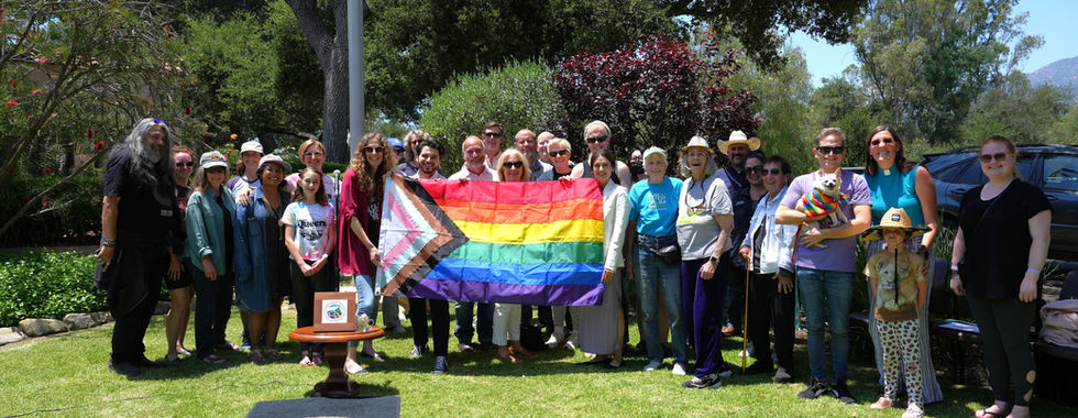 A photograph of a group of people holding a progress pride flag on a grassy lawn