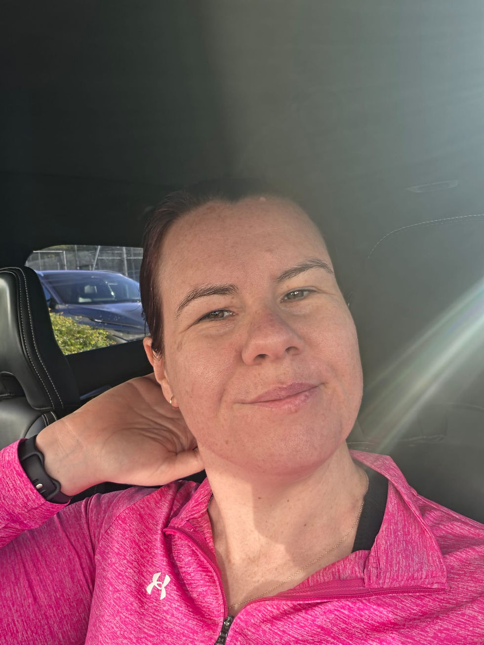 Woman sat in car wearing a pick gym top, smiling. Selfie photo.