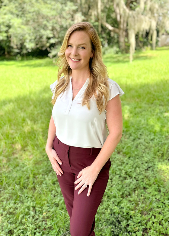 Blonde woman standing in grass smiling wearing business attire
