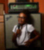 photo of a child infront of a large amp, smiling while singing into a microphone