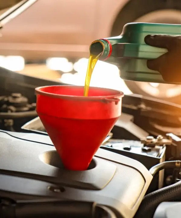 A person pouring oil from a dark green canister into an engine with a red funnel
