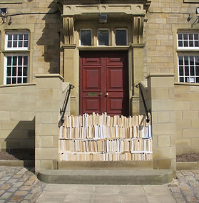 An old fashioned looking building with a wooden door. Books are neatly stacked up in front of the door, blocking the entryway