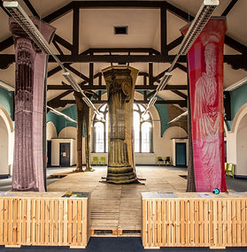 A large room with two floor to ceiling pillars, they are covered in a knitted cover showing a representation of an old greek style column