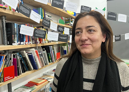 Ayesha Butt, a young woman with light briwn skin and brown hair is stood infront of bookshelves