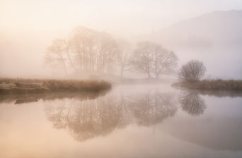 Early morning mist rolls across the river Brathay in Langdale, the Lake District creating an ethereal scene.