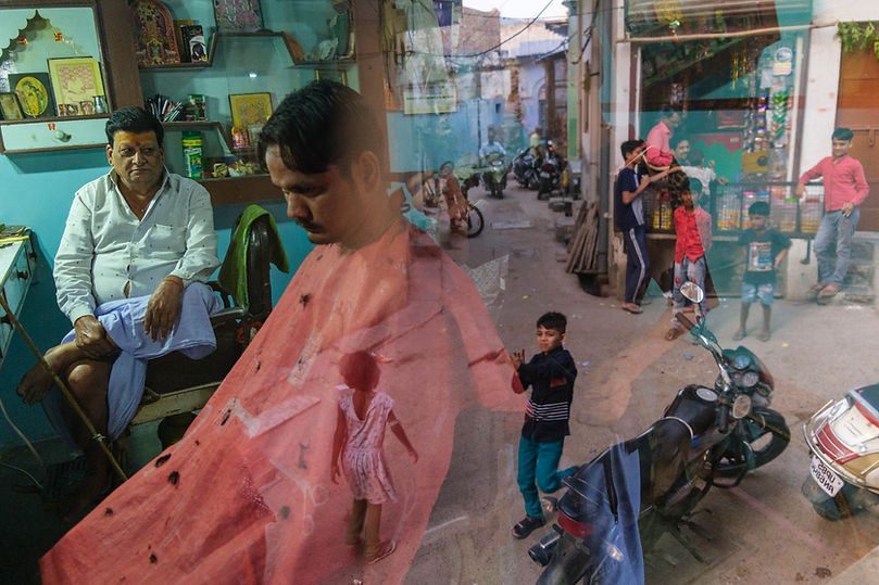 Barber_A man is giving a haircut to a customer while children are playing on the street