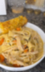 Eye-level view of a steaming bowl of chicken noodle soup with fresh herbs and egg noodles