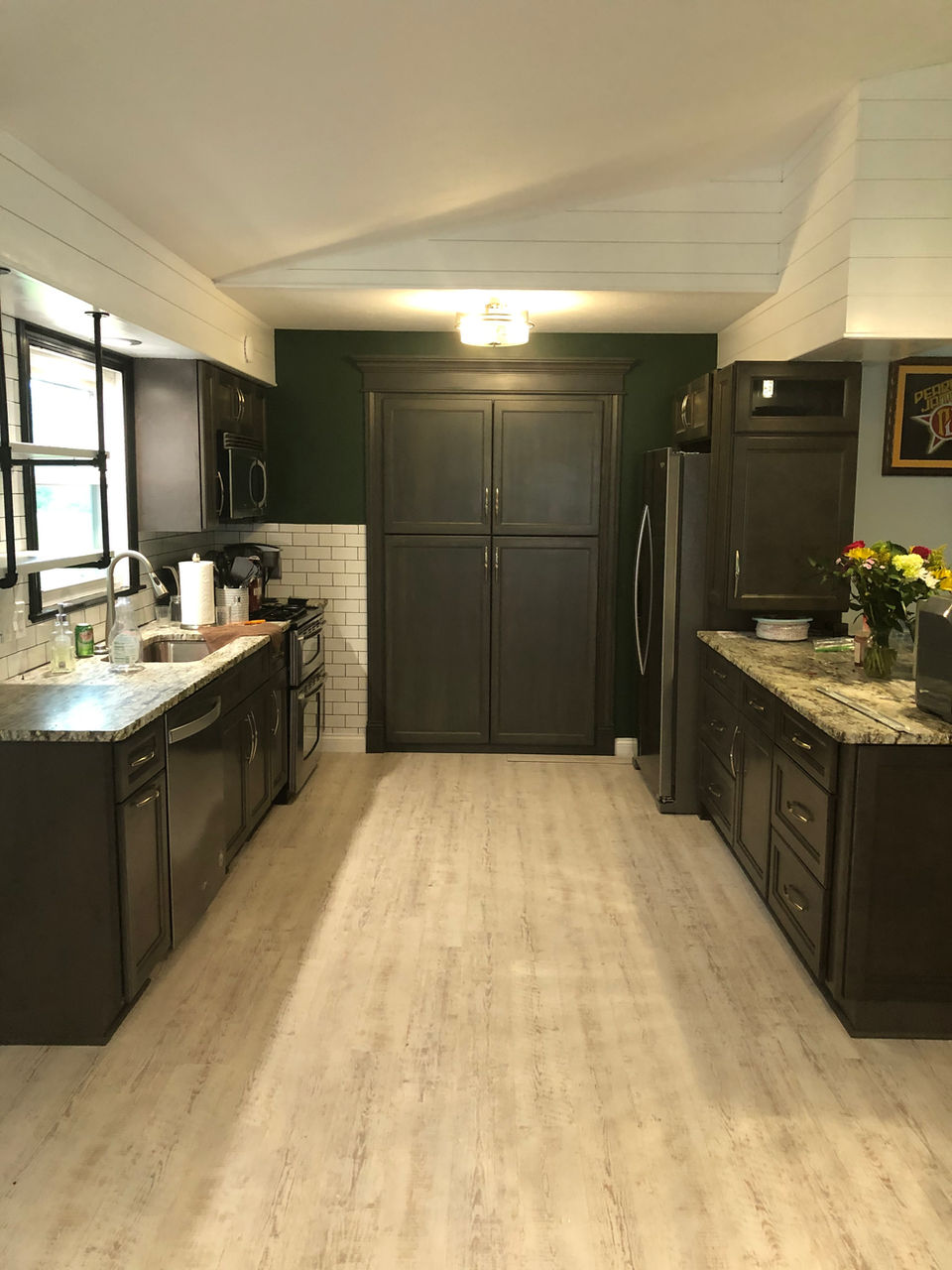 A dated kitchen is being transformed into a sleek, contemporary space. Dark, modern cabinetry provides a sophisticated backdrop, while a rich green accent wall adds a touch of personality. A clean white tiled backsplash and sleek black hardware complete the stylish and functional design.