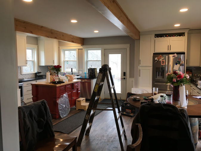 They are transforming their kitchen into a rustic yet stylish space. Featuring exposed wooden ceiling beams, classic red brick walls, and crisp white cabinetry, the kitchen will exude a warm, inviting atmosphere. A bold red island adds a pop of color that complements the home's exterior.