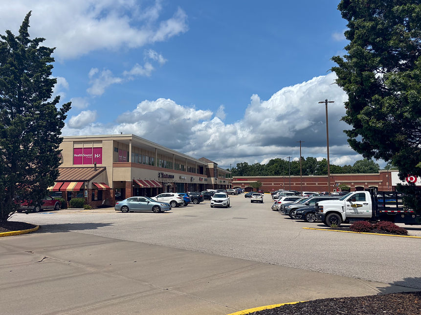 Exterior view of businesses and parking lot under blue skies and clouds.