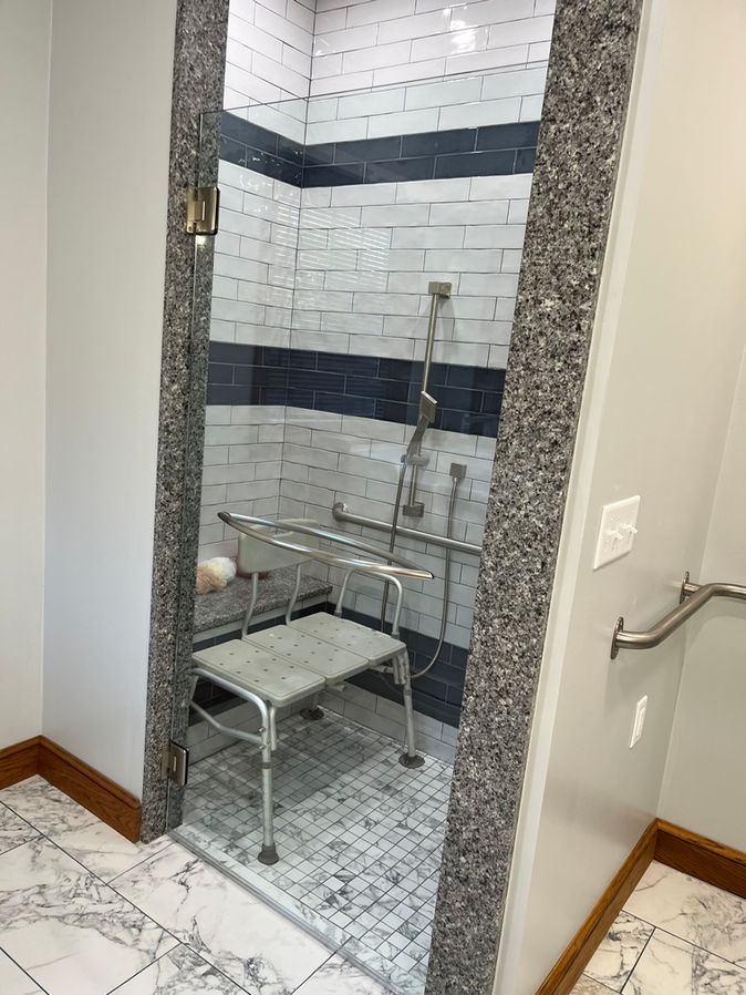 This master bathroom is undergoing a complete overhaul is being redesigned with accessibility in mind. The renovation includes installing elegant white marble tile flooring throughout the space. The new shower and bath incorporates handicap-friendly features. along with a hand railing for completed touch.