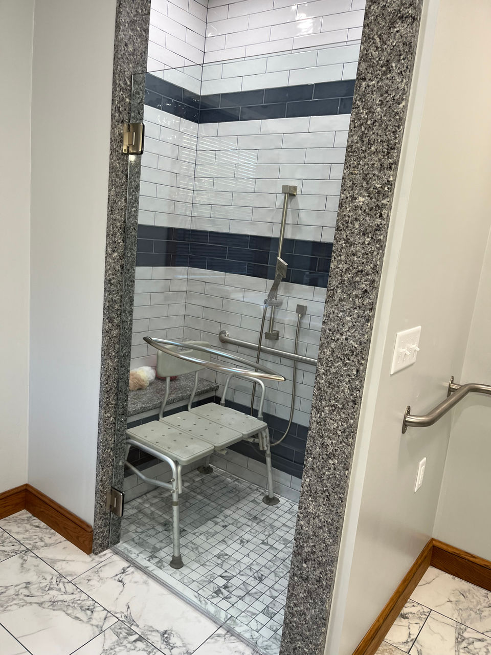 This master bathroom is undergoing a complete overhaul is being redesigned with accessibility in mind. The renovation includes installing elegant white marble tile flooring throughout the space. The new shower and bath incorporates handicap-friendly features. along with a hand railing for completed touch.