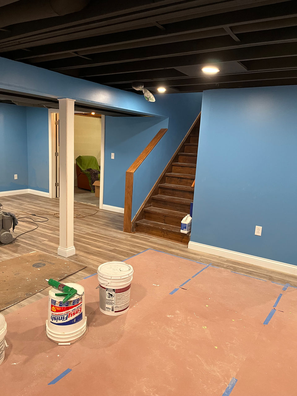 A stylish and modern basement remodel. The design features a black ceiling, blue walls, and warm grey wood flooring. This combination promises a fun and inviting atmosphere for the finished basement.